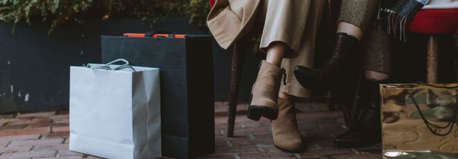 Shopping bags by a person's legs as they sit on a chair.