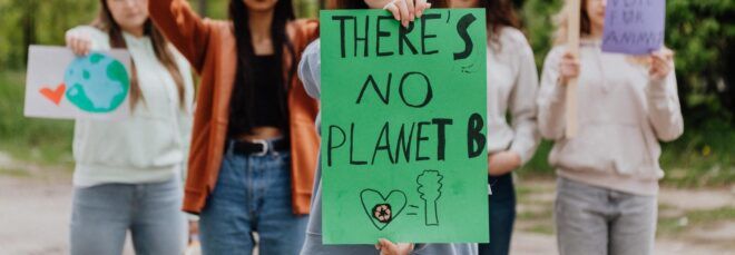A group of protesters with one person in front holding a green sign reading "there's no planet B."