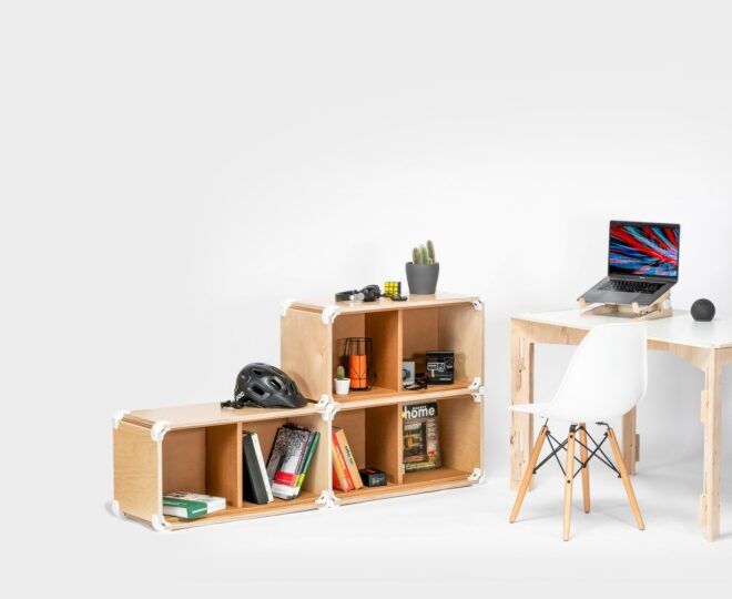 A shelf next to a wood desk that has an open laptop on it and a white chair in front of it in a white room