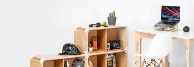 A shelf next to a wood desk that has an open laptop on it and a white chair in front of it in a white room