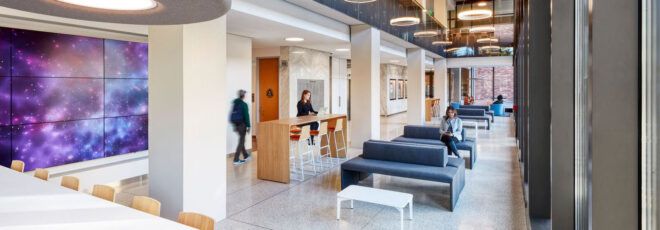 A lobby area where people sit on sofas and at tables, with a galaxy mural to the left.