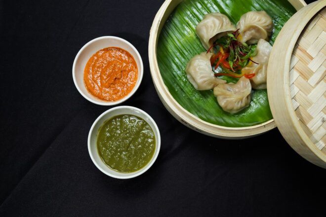 A basket of dumplings with a side of orange sauce and green sauce