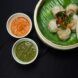 A basket of dumplings with a side of orange sauce and green sauce