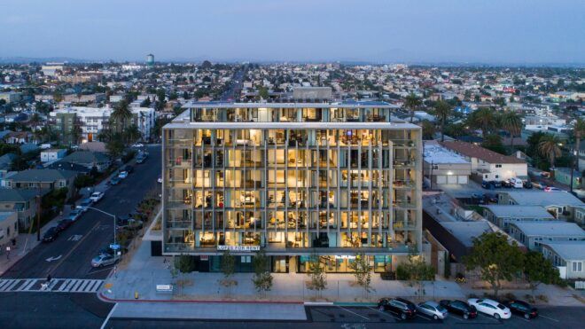 A square shape building lit with lights from within set against a city
