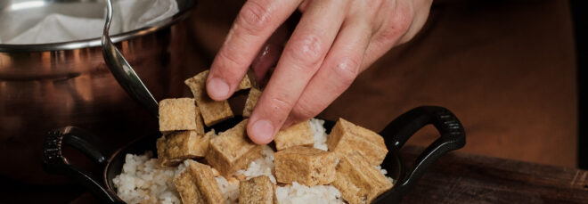 A hand setting a bowl filled with rice and tofu