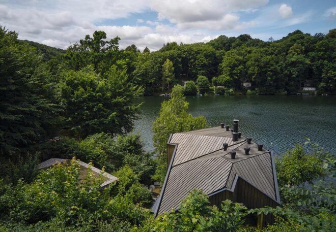 A home peaking out from the trees by a lake.