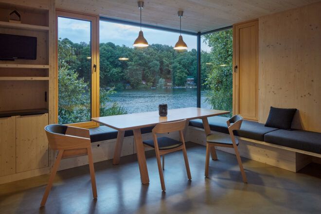 A minimalist dining room with wood floors, walls, table and chairs next to a large window.