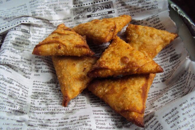 Triangle-shaped deep fried food wrapped in a newspaper