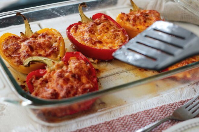 Stuffed bell peppers in a glass tray with a metal spatula touching them