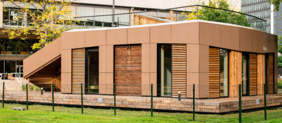 Wood clad house with tan-colored solar panels on the facades and an open roof garden