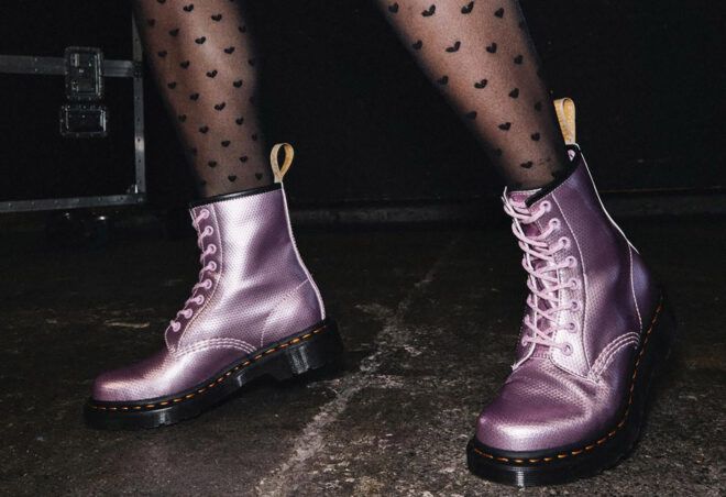 A person in sheer black tights wearing a pair of pink Dr. Martens.