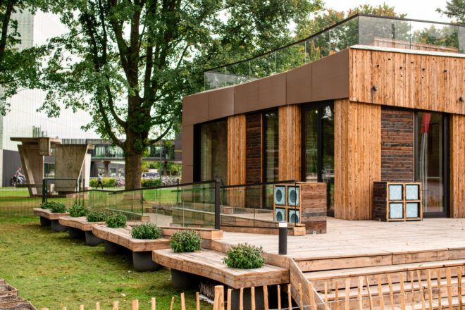 Corner view of wood clad house on a wooden deck next to benches that have in-built planters