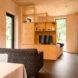 View across a desk towards a living space with shelving and a bed at the back facing a floor-to-ceiling window