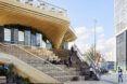 The exterior of a two-level wood pavilion with an outdoor staircase leading inside.