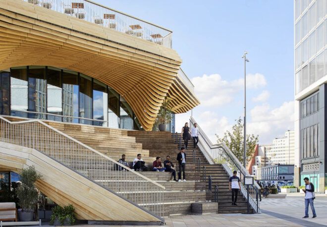 The exterior of a two-level wood pavilion with an outdoor staircase leading inside.