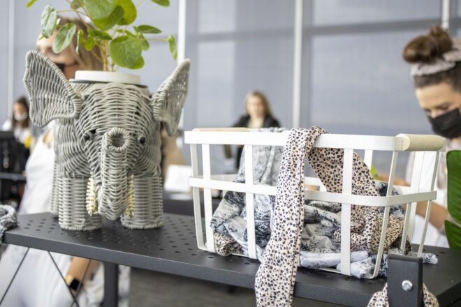 A wire elephant holding a potted plant beside a basket of patterned scarves