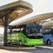 A green bus and a blue bus stationed underneath an overhang
