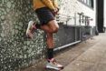 A pair of legs against a wall, wearing mulitcolor Adidas shoes.