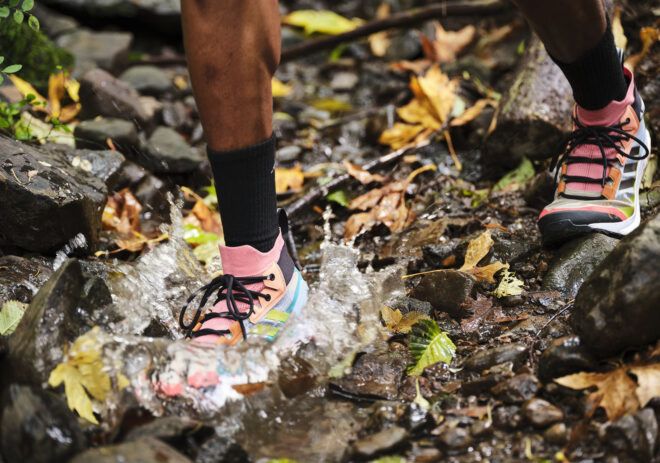 A foot wearing multicolor sneakers splashing in a puddle in the woods.