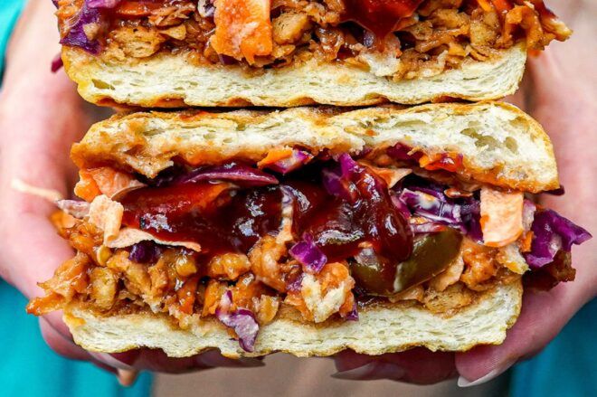 Two hands holding a sandwich loaded with meats and vegetables