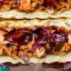 Two hands holding a sandwich loaded with meats and vegetables