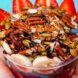 A hand holding a smoothie bowl loaded with nuts, strawberries and banana slices against a blue background