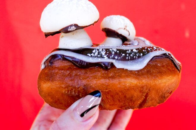 A hand holding a donut that is covered in edible mushroom creations