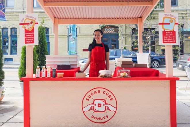 A pink bakery stand with a woman wearing a red apron standing inside of it