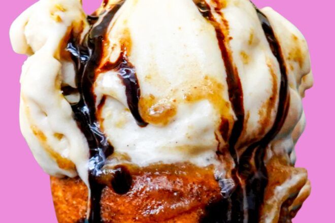 Close up of an ice cream cone dripping chocolate and caramel syrup against a pink background