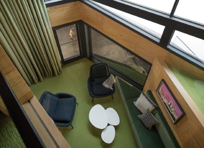 A living room with green carpet, two blue chairs, and a white coffee table with green curtains