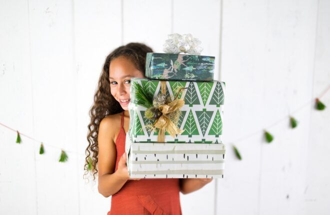 A girl with curly hair holding three boxes of gifts stacked on top of each other