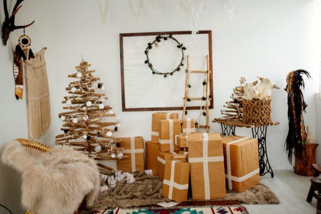 A wooden Christmas tree made of logs with presents sitting next to it wrapped in brown paper and white ribbon