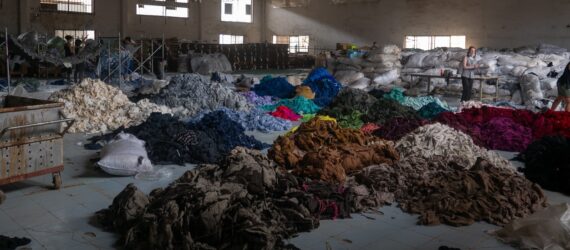 A large warehouse with piles and piles of clothes on the ground