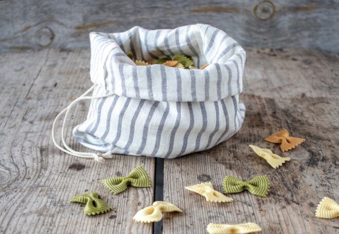 A fabric bag with dried pasta in it and spread outside of it