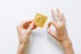 Two hands, one of them is holding up a condom in its wrapper while the other hands has it in a signal of OK