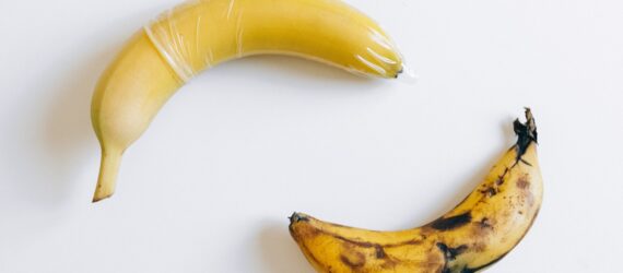Two bananas with one of them has a condom on it while the other one is browning and doesn't have a condom