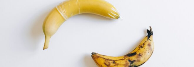 Two bananas with one of them has a condom on it while the other one is browning and doesn't have a condom