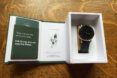 An opened green and white box with a black watch inside.