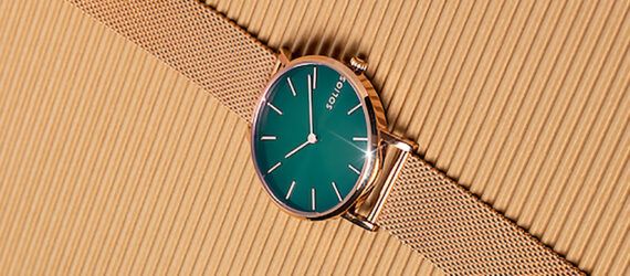 A green and copper watch on a beige background.