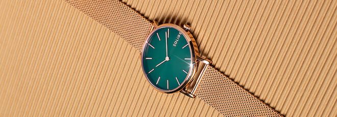 A green and copper watch on a beige background.