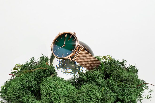 A green and gold watch on a bed of moss.