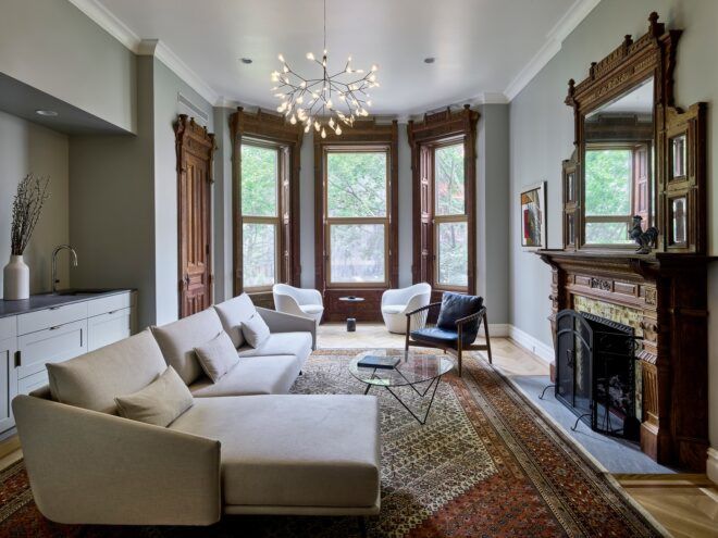 A living room with a long sofa in front of a fireplace and windows in the far distance