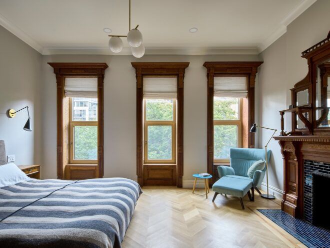 A bed room with three rectangle windows against the wall and a blue chair in the corner