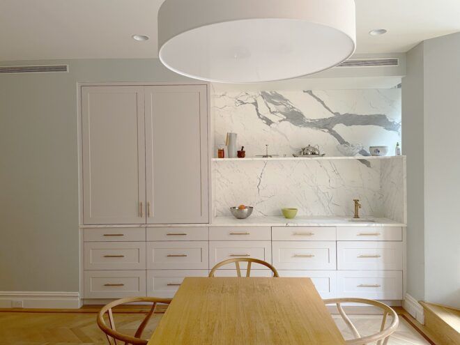 A dining room area with white shelves and cupboards and a wooden table with three chairs in front of it