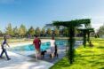 People walking beside a pool with a pole trellis put on the grass surrounding the pool