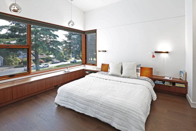 A white bedroom with wood accents around a large window.