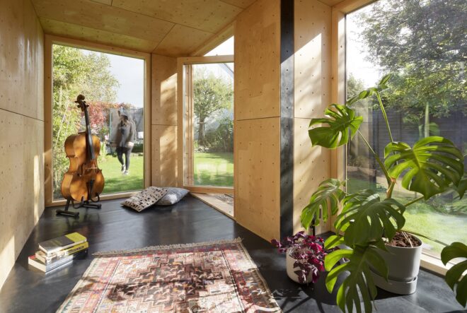 The interior of the dwelling unit has a cello in the corner and windows all around