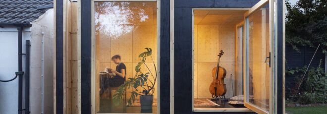 Glass windows with a person inside sitting on a chair with a cello beside them