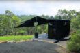 A driveway area leading up to a black house on a green hill.