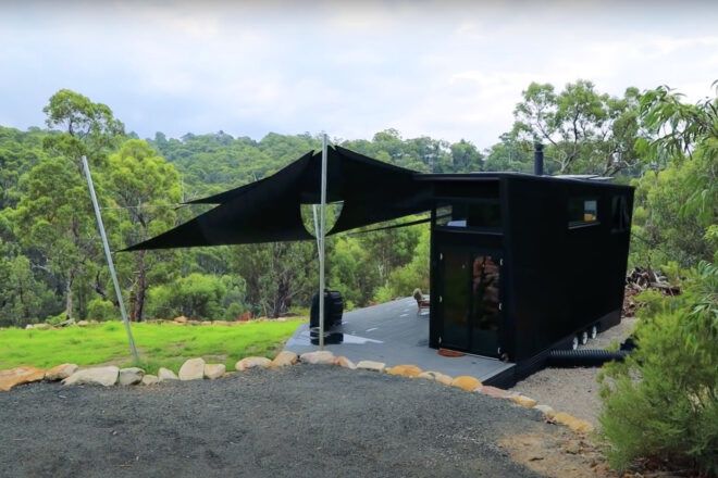 A driveway area leading up to a black house on a green hill.